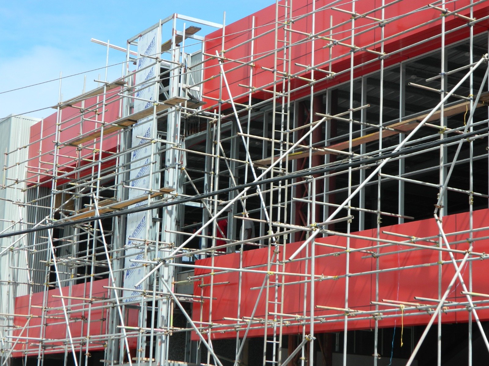 Red aluminium composite panel bands being installed behind scaffolding